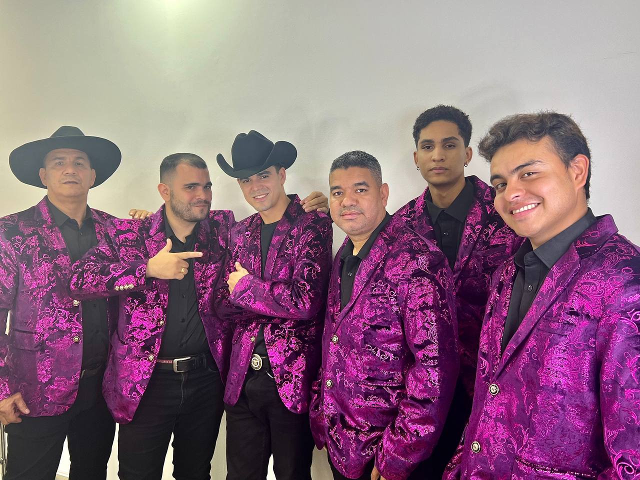Integrantes de Arrieros Banda vistiendo trajes regionales mexicanos elegantes de color morado con negro
